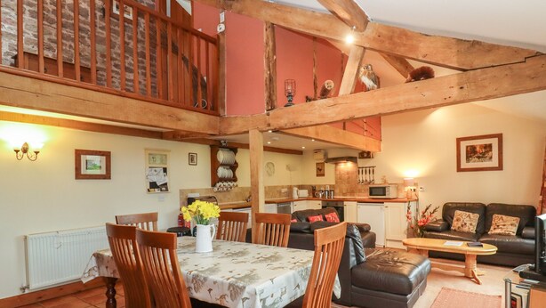 A spacious living area with a dining table, chairs, a sofa, and a kitchen in the background. - The Old Stables (Ross-on-Wye)