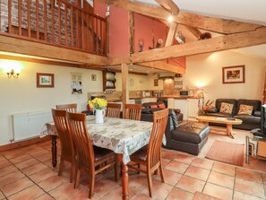 A spacious living area with a dining table, chairs, a sofa, and a kitchen in the background. - The Old Stables (Ross-on-Wye)