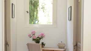 Ein schmaler Korridor mit einem Fenster, einem Stuhl, einem kleinen Tisch und einer Tür.