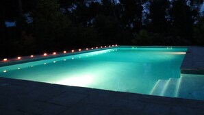 Ein Schwimmbecken im Abenddämmerung mit Beleuchtung am Rand.