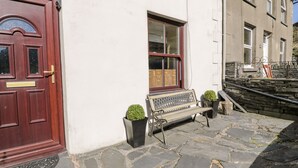 A stone-paved entrance with a red door, a bench, and two potted plants. - Miners Cottage (Blaenau Ffestiniog)