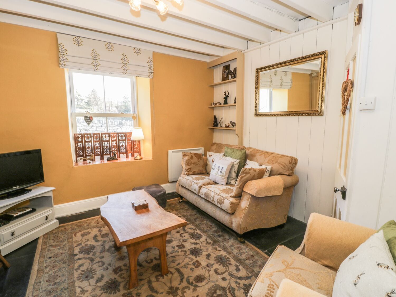 A living room with a sofa, a coffee table, a television, and a window with a view of trees.