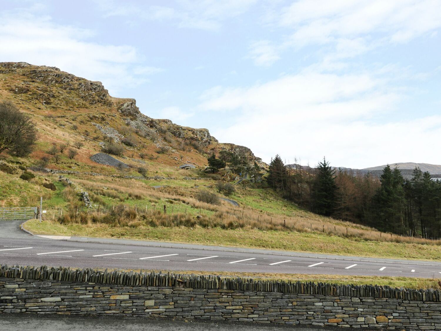 Una carretera rural serpentea por un paisaje montañoso con muros de piedra y vegetación escasa.