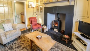 A cozy living room with a fireplace, a sofa, a red polka dot chair, a wooden coffee table, and a television on a white stand. - Miners Cottage (Blaenau Ffestiniog)
