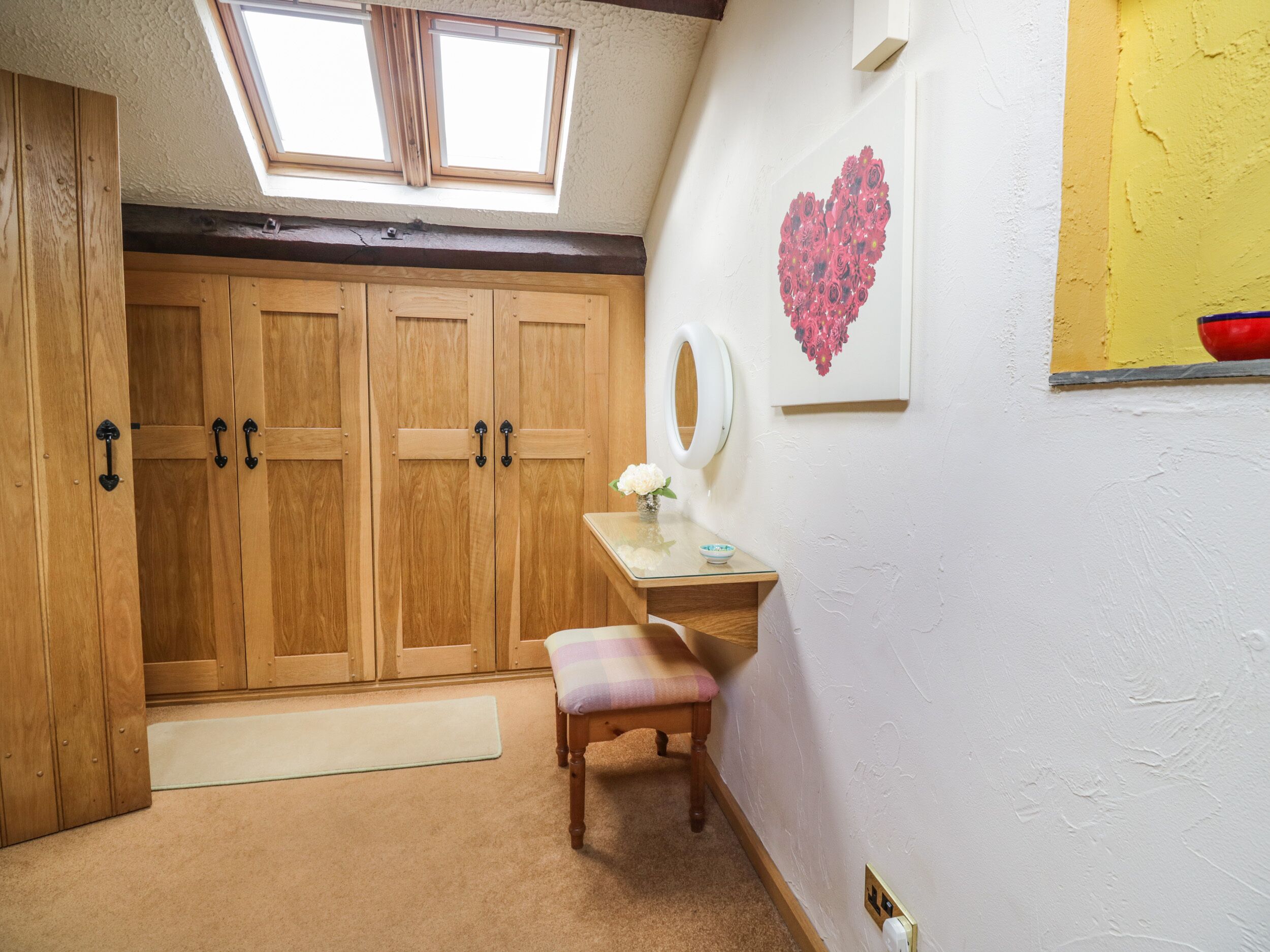 A room with a skylight, wooden wardrobe, a vanity with a mirror, and a heart-shaped artwork on the wall.