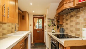A compact kitchen with wooden cabinets, a built-in oven, and a countertop with a kettle. - The Cottage at Graysondale Farm (Cockermouth)