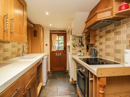 Una cocina compacta con armarios de madera, horno empotrado y una encimera con hervidor.