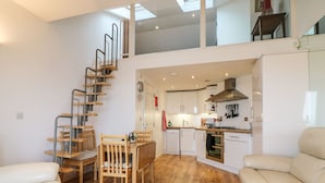 Un apartamento moderno con escalera de madera, comedor, cocina y sala de estar con sofá.