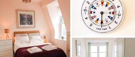 A bedroom with a bed, bedside tables, and a window. There is a wall-mounted tide chart.