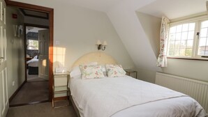 A bedroom with a bed, a nightstand, a lamp, a window with curtains, and a door leading to another room. - The Lodge off High Street (Ipswich)