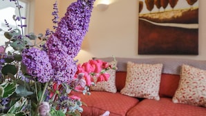 Un salon avec un canapé, des coussins décoratifs et un arrangement floral.