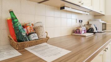 A kitchen counter with a basket containing a green bottle, a red bottle, and various food items. There is a microwave and a toaster on the counter.