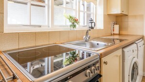 Une cuisine équipée d’une cuisinière, d’un évier et d’un lave-vaisselle. Une fenêtre offre une vue sur un bâtiment en briques.