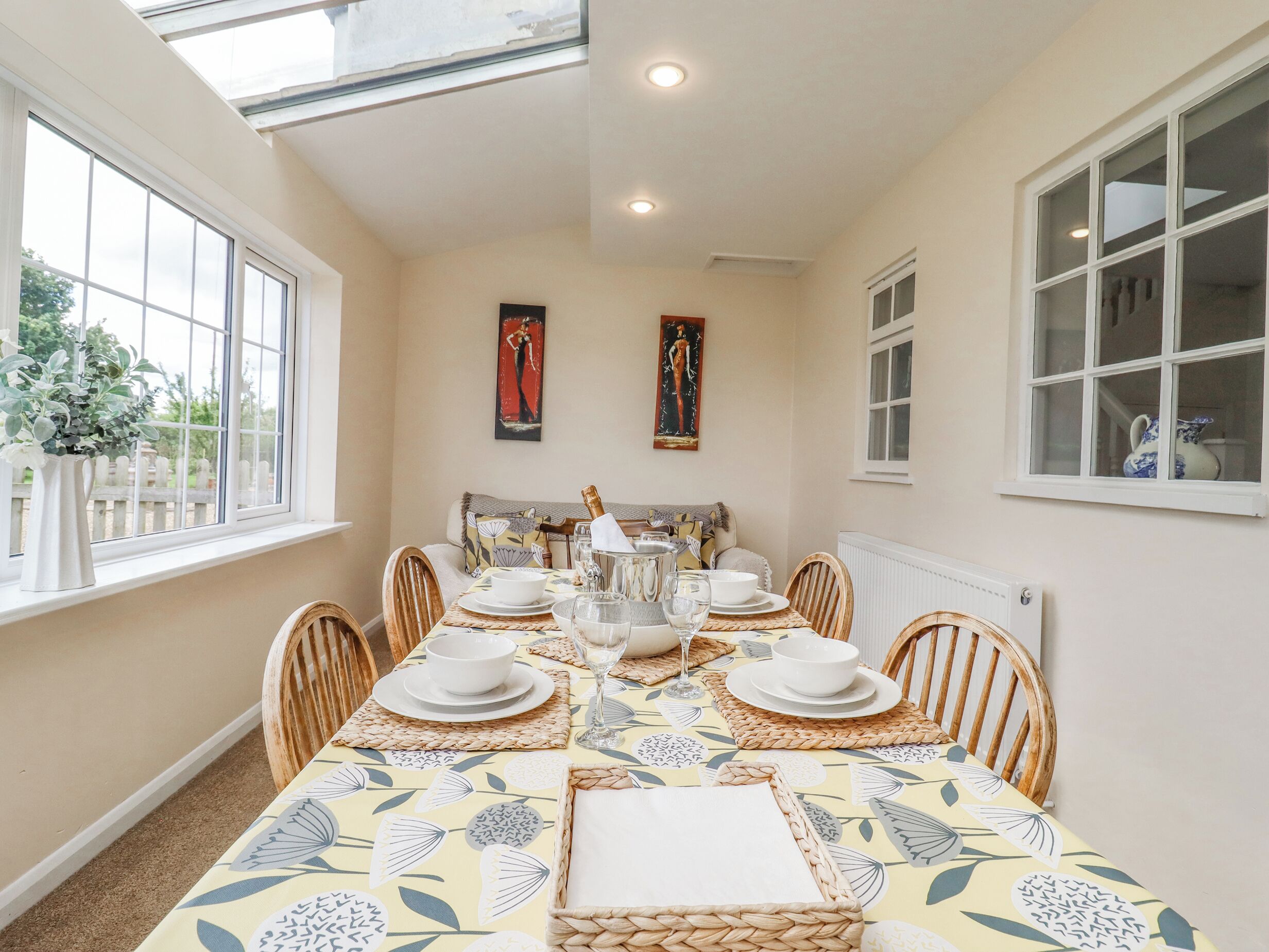 Comedor con una mesa dispuesta para cuatro, con mantel estampado, platos blancos y una botella de champán.