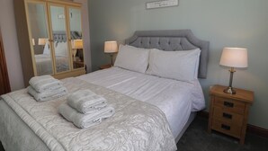 Un lit bien fait, avec une tête de lit, deux lampes de chevet, une table de nuit en bois, une armoire à miroir et un cadre avec une citation accroché au mur.