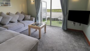 Un salon moderne avec un canapé gris, une petite table en bois et un téléviseur à écran plat fixé au mur.