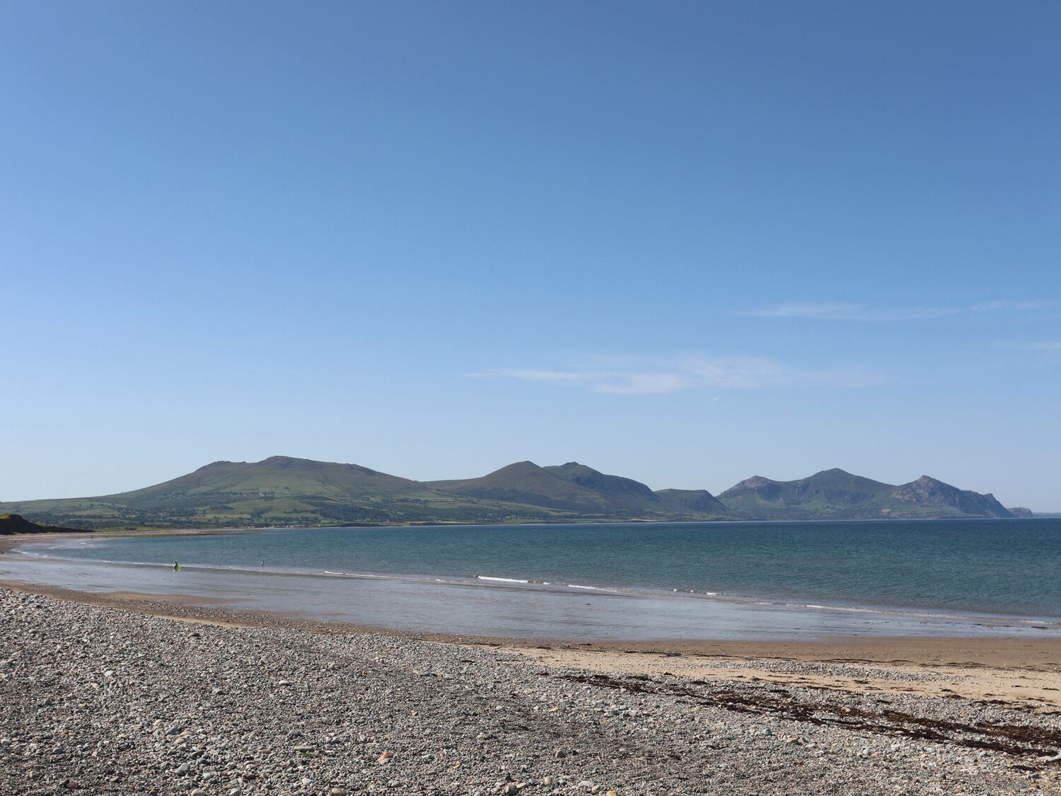A pebbly beach with distant mountains under a clear sky.