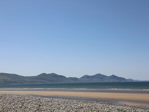 Uma praia com um primeiro plano rochoso e montanhas ao fundo.