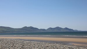 En strand med en stenig förgrund och berg i bakgrunden.