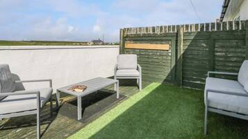 A rooftop patio with two white chairs, a small table, and a book. The patio has artificial grass and a wooden deck.