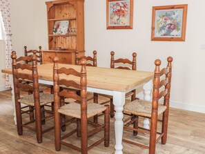 A dining room with a wooden table and chairs, a wooden cabinet, and two framed floral paintings on the wall. - East Lodge (Walkerburn)