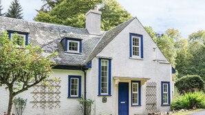 A traditional white house with blue trim and a steeply pitched roof, surrounded by greenery. - East Lodge (Walkerburn)