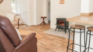 A living room with a brown leather sofa, a wooden floor, a black wood-burning stove, and a small round table. - East Lodge (Walkerburn)