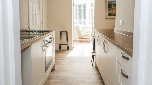A kitchen with a wooden countertop, white cabinets, and a view to a balcony. - East Lodge (Walkerburn)