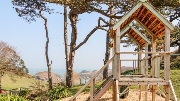 Une tour d’observation en bois, dotée d’un escalier et d’une plateforme panoramique, entourée d’arbres et offrant une vue sur un paysage pittoresque.