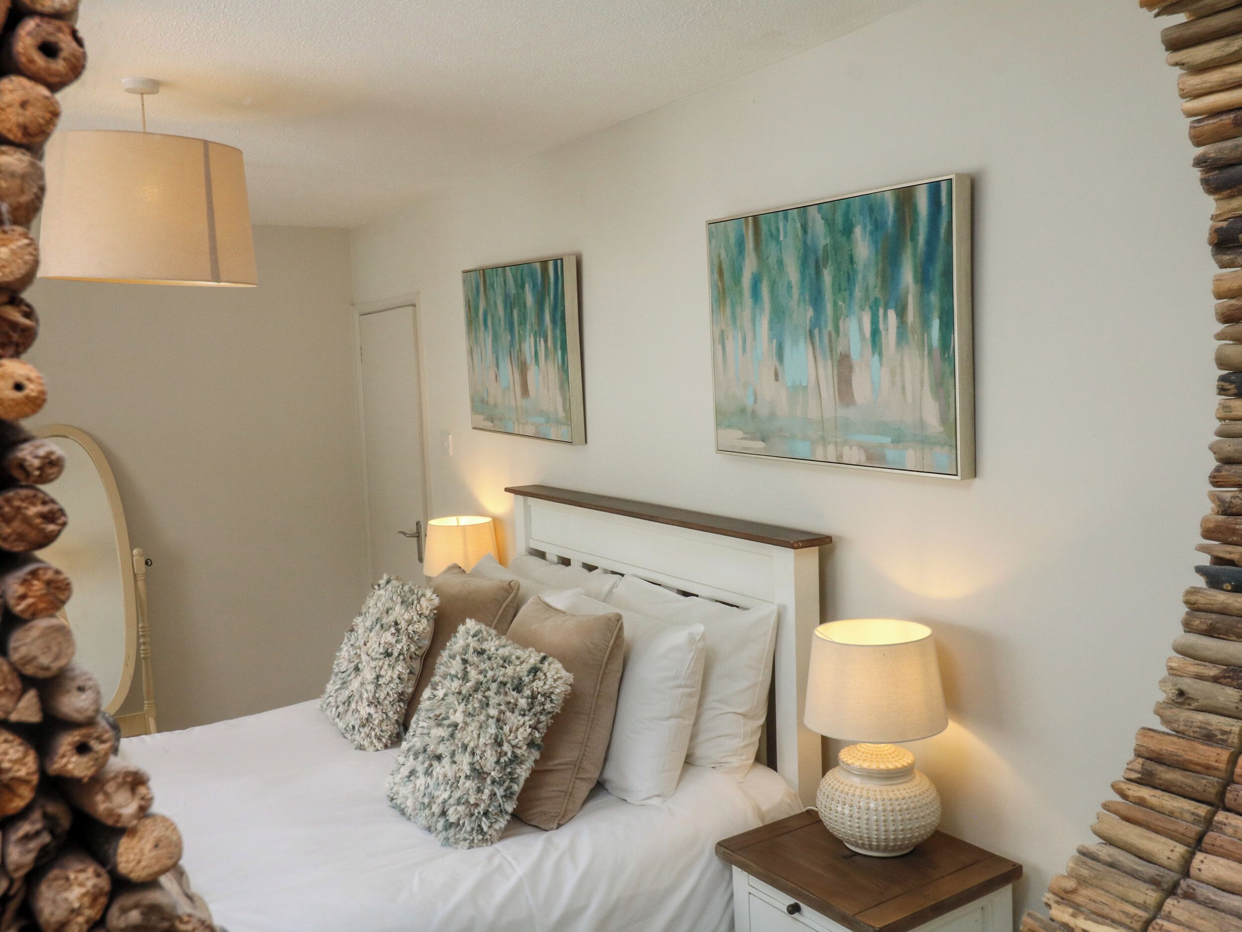Een netjes ingerichte slaapkamer met een bed, twee aan de muur bevestigde schilderijen, een bedlampje en een houten nachtkastje.