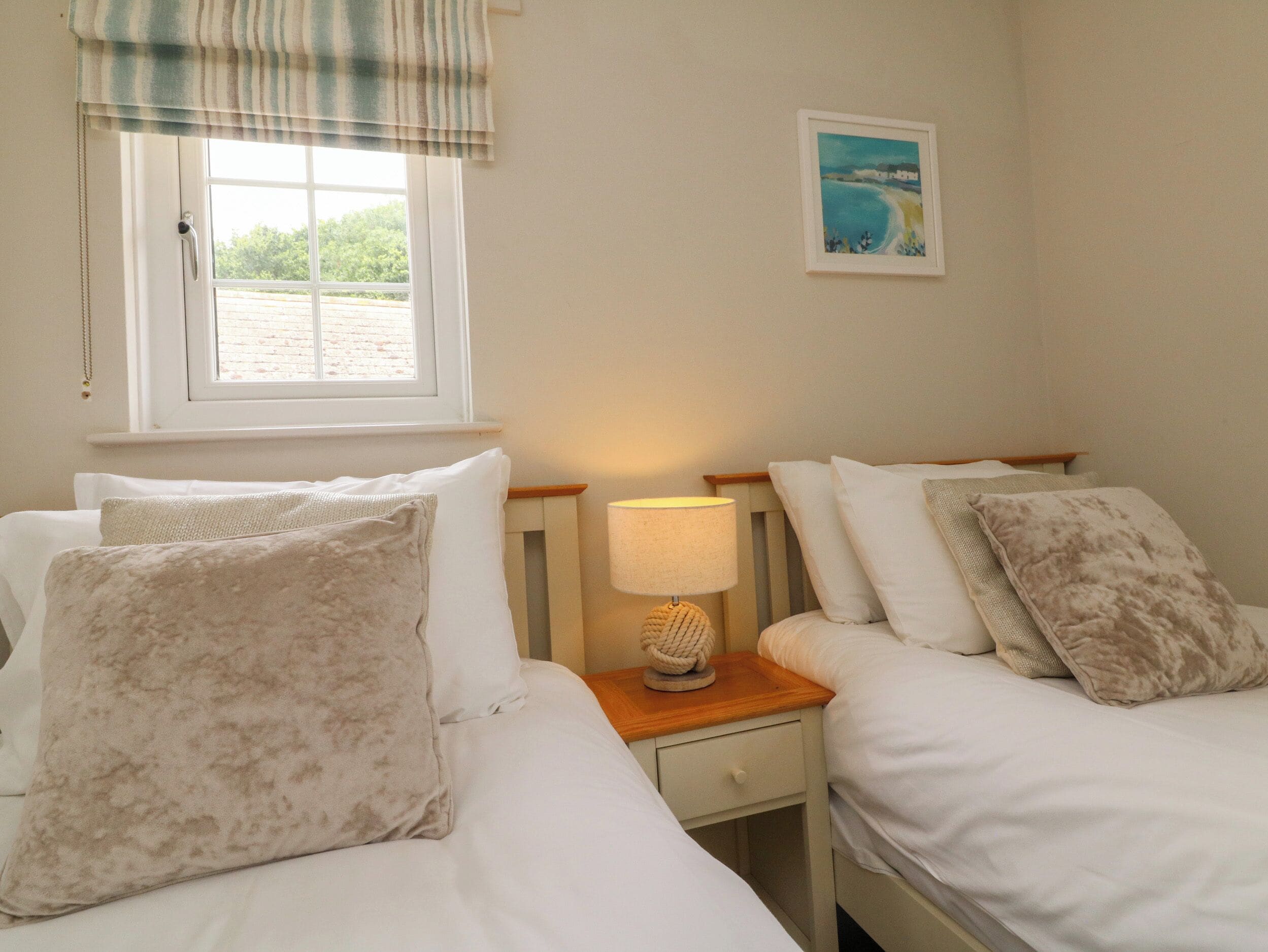 Een slaapkamer met twee bedden, een raam met uitzicht, een bedlamp en een schilderij aan de muur.