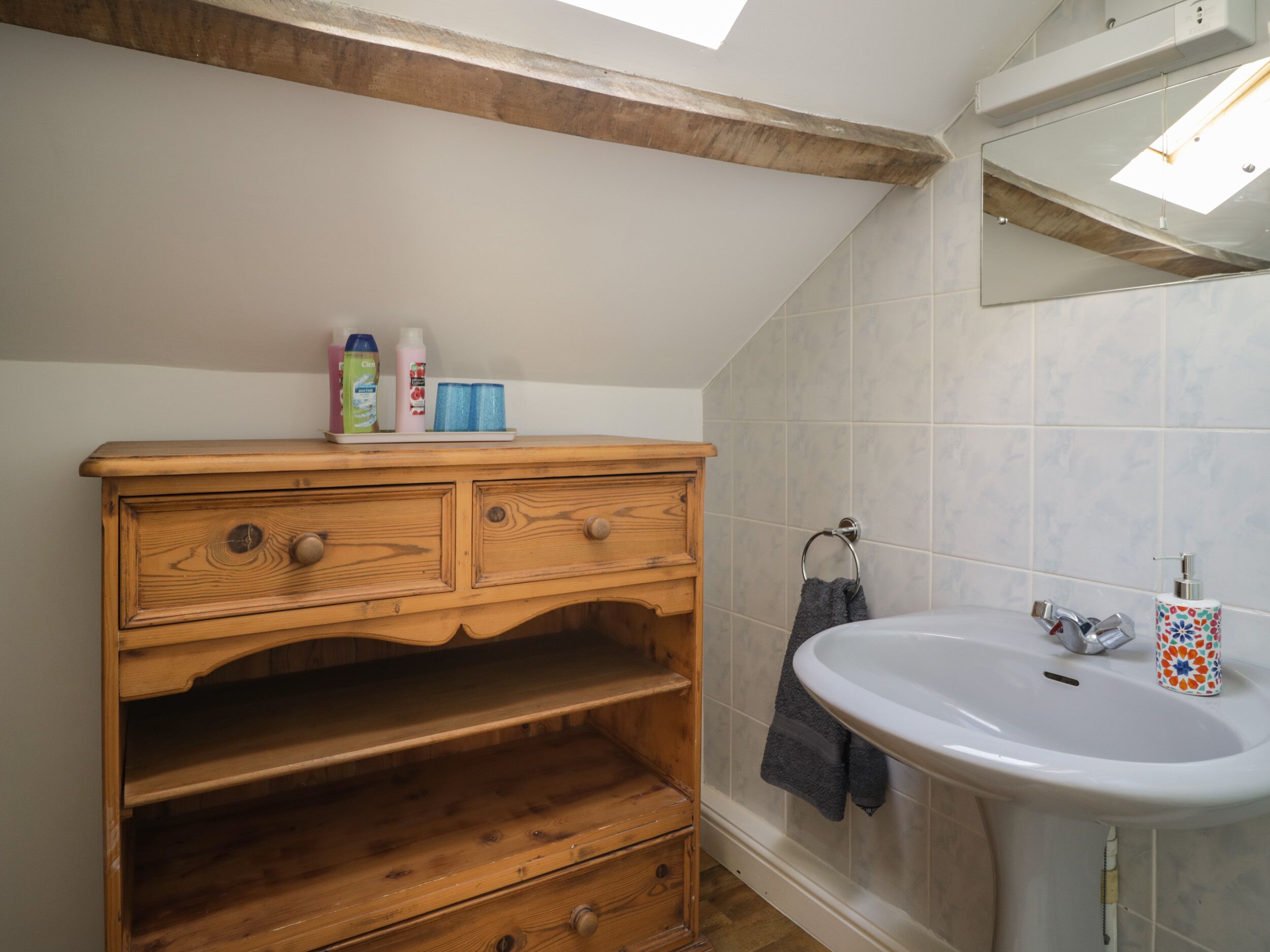 A bathroom with a wooden vanity, a white sink, and a skylight.