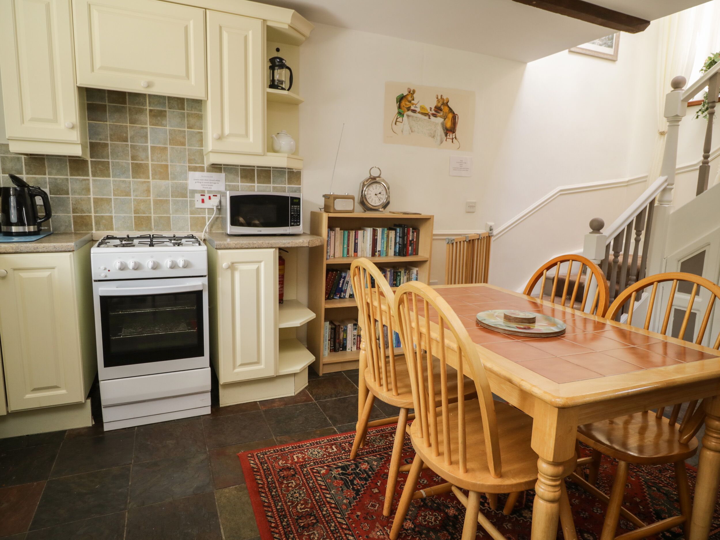 A kitchen with white cabinets, a stove, a microwave, a bookshelf, and a dining table with chairs.