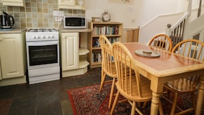 A kitchen with white cabinets, a stove, a microwave, a bookshelf, and a dining table with chairs. - Mousehole Cottage (Carlisle)