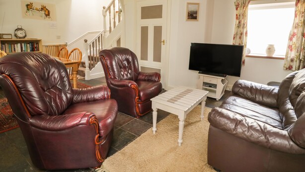 A living room with leather armchairs, a sofa, a television, and a staircase. - Mousehole Cottage (Carlisle)
