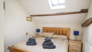 A bedroom with a wooden bed, two bedside tables with lamps, a skylight, and a small shelf with decorative items. - Mousehole Cottage (Carlisle)