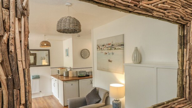 A cozy room with a rustic mirror frame, a comfortable chair, a lamp, and a kitchen area with a microwave and toaster. - Wren Cottage (Ilfracombe)