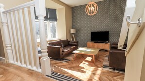 Ein Wohnzimmer mit einem braunen Ledersofa, einem Glastisch, einer Holz-TV-Konsole und einer Wand mit Musterung.