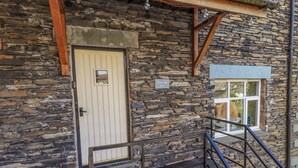 Ein Steinhaus mit einer Holztür, einem kleinen Fenster und einer Metalltreppe.