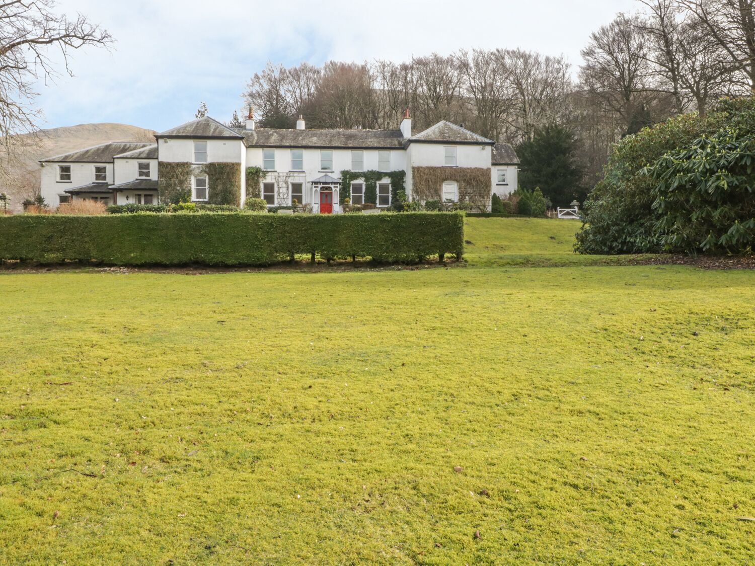 A large, white building with multiple windows and a red door, surrounded by a well-maintained lawn and hedges.