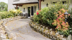 A stone pathway leading to a white building with a covered entrance and outdoor seating. - Thirlmere Suite (Keswick)