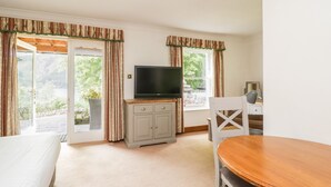 A room with a bed, a TV on a cabinet, a dining table, and a window with curtains. - Thirlmere Suite (Keswick)