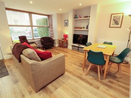 A living room with a sofa, a dining table with chairs, a TV, and a bookshelf.