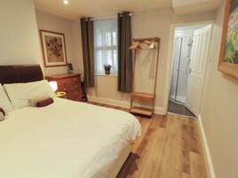 A bedroom with a bed, dresser, window with curtains, and a door leading to another room.
