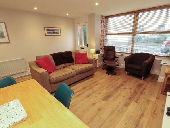 A living room with a sofa, two armchairs, a wooden dining table, and a window with blinds. - Archers (Keswick)