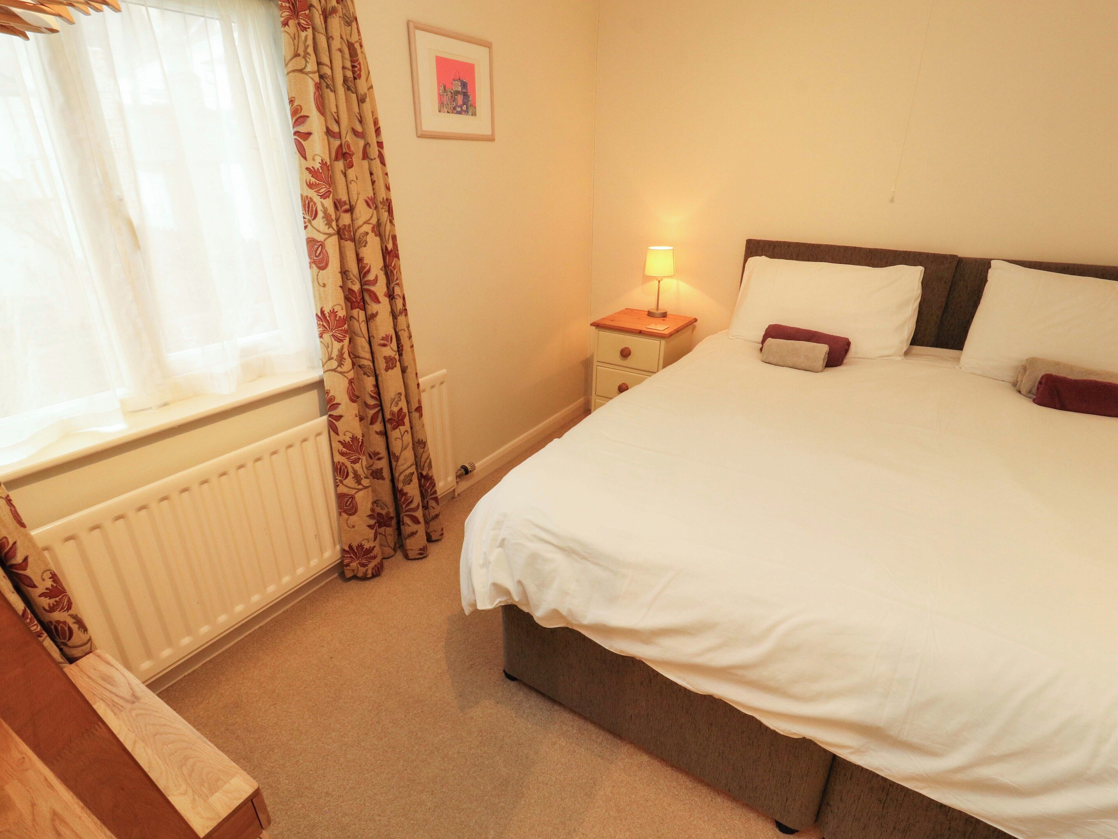 A hotel room with a bed, a nightstand with a lamp, a radiator, and curtains.