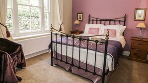 A bedroom with a four-poster bed, a window with curtains, a nightstand, and a dresser. - Rowan Cottage (Ambleside)