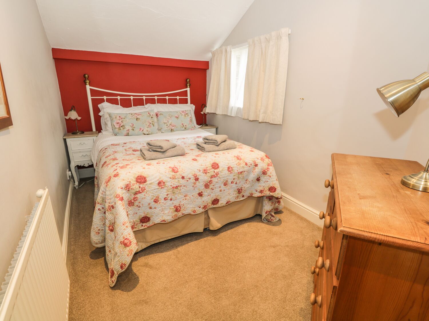 A bedroom with a bed, a nightstand, a wooden dresser, and a radiator.
