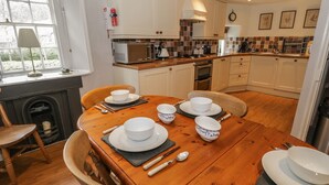 A cozy kitchen with white cabinets, a wooden dining table set with white and blue patterned bowls, plates, and cutlery. - Rowan Cottage (Ambleside)