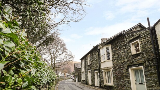 A narrow street lined with stone buildings, some with bay windows, and a stone wall on one side. - Rowan Cottage (Ambleside)